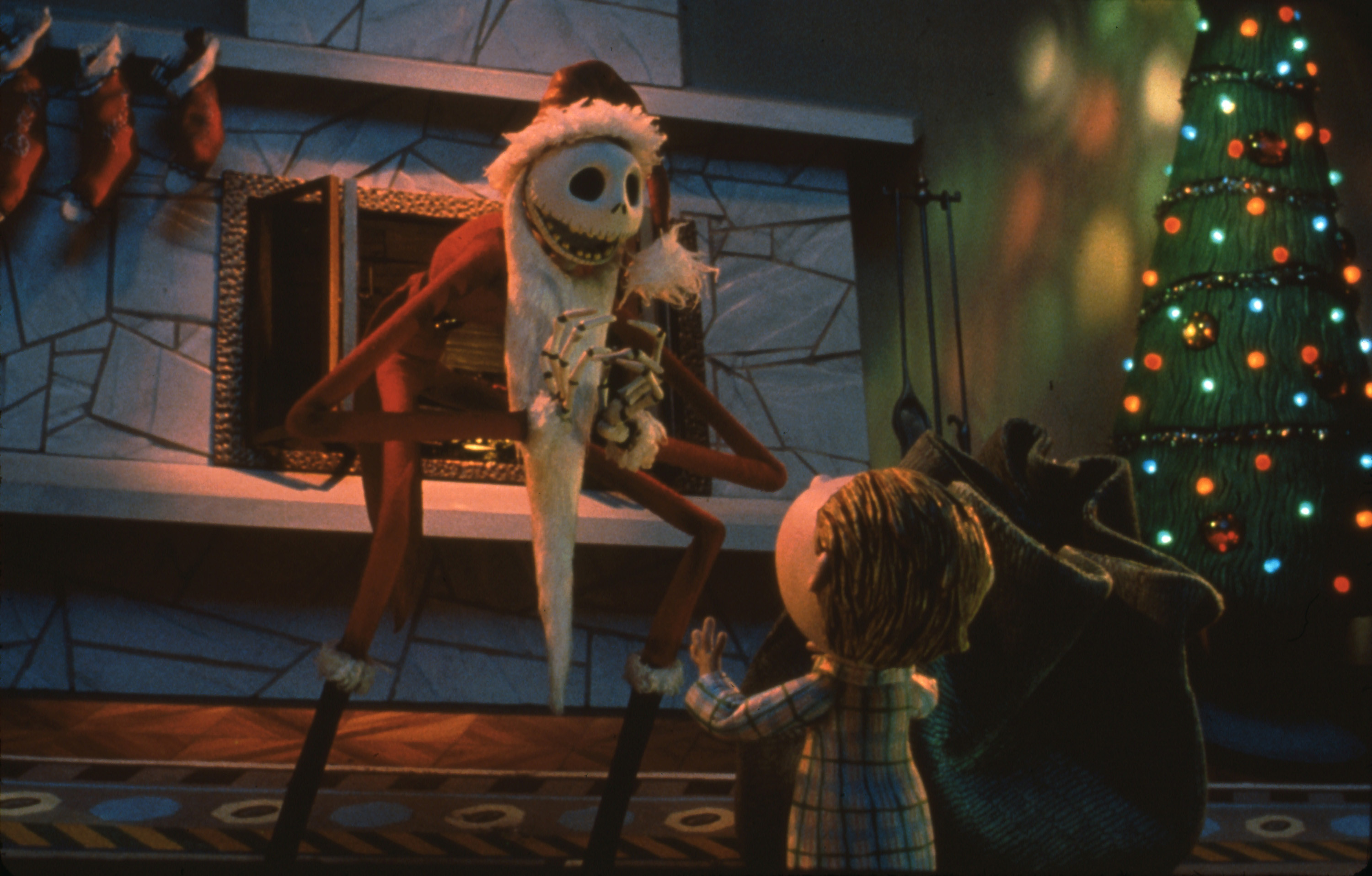 Personagem Jack Esqueleto vestido de Papai Noel em frente à lareira e árvore de Natal iluminada