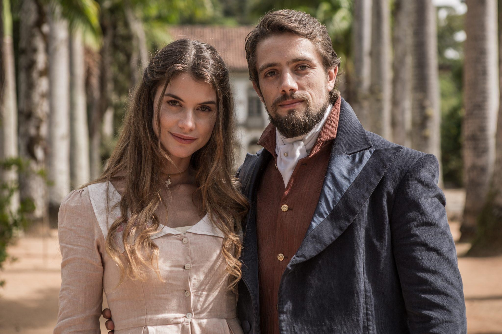 Casal em trajes de época posando ao ar livre na novela Além do Tempo.