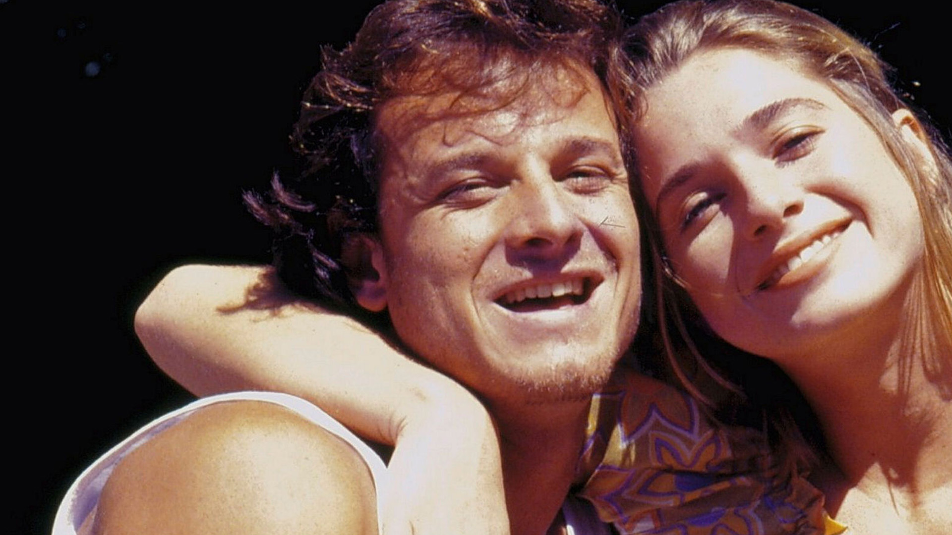 Casal sorridente se abraçando em cena da novela Quatro por Quatro.
